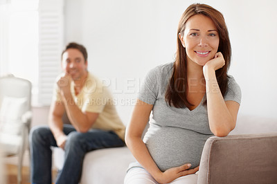 Buy stock photo Portrait of a pretty young pregnant woman with her spouse sitting in the background