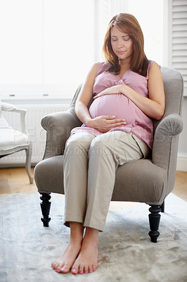 Buy stock photo A glowing pregnant woman looking at her swelling baby bump