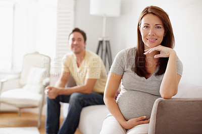 Buy stock photo A beautiful pregnant woman holding her stomach while her husband sits in the background
