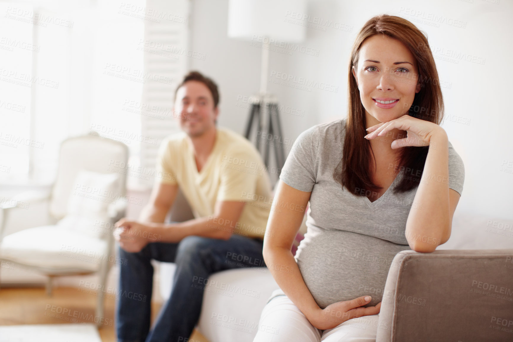 Buy stock photo A beautiful pregnant woman holding her stomach while her husband sits in the background