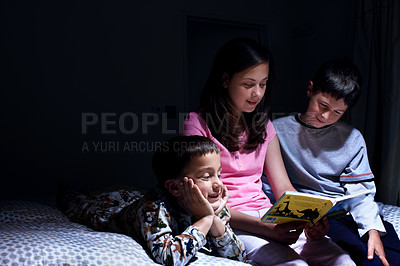 Buy stock photo A sister reading to her younger brothers by lamplight in the bedroom - Copyspace