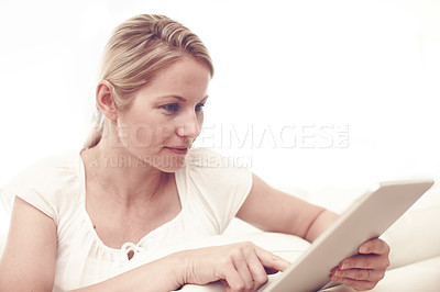 Buy stock photo An attractive blonde woman using a tablet while sitting at home