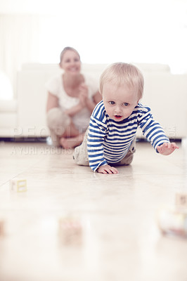 Buy stock photo A cute baby boy crawling on the floor as his proud mother looks on