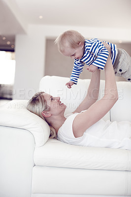 Buy stock photo Cropped view of an attractive young mother lifting her cute baby boy as she lies on the sofa