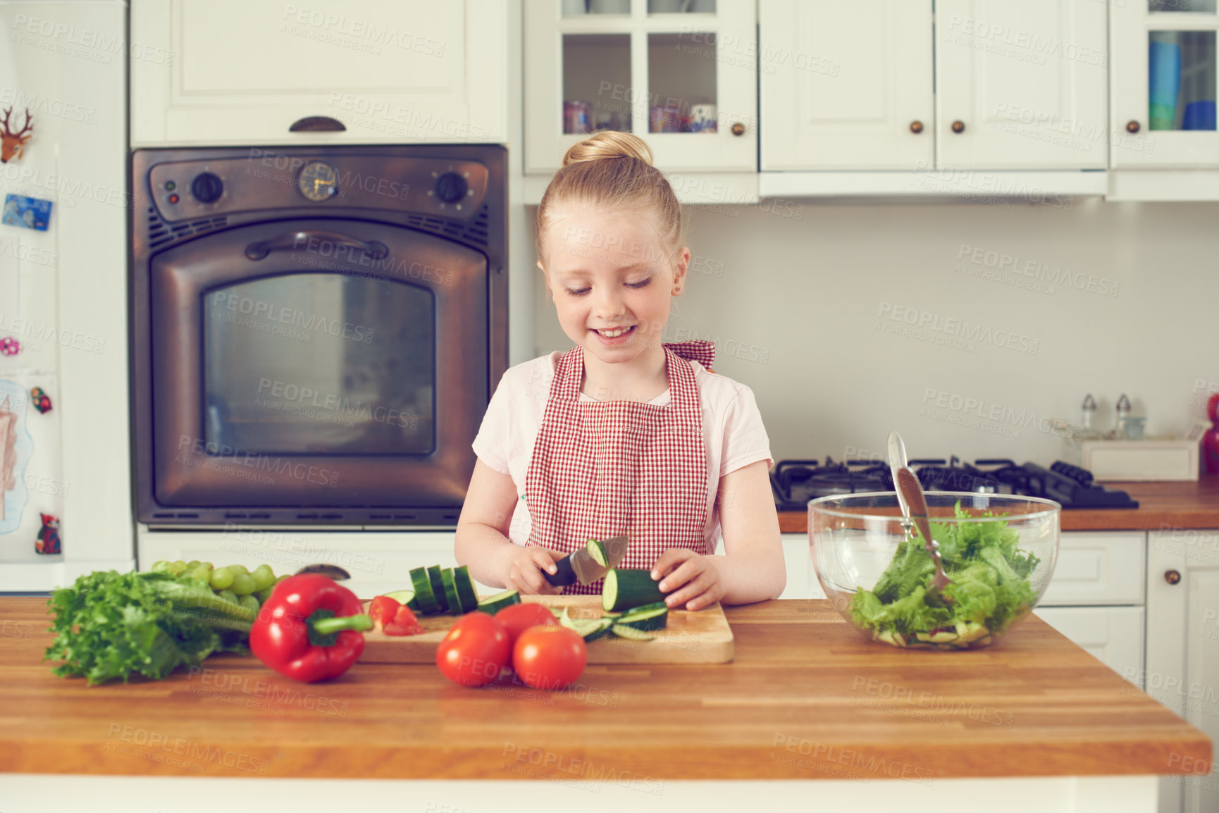 Buy stock photo One happy girl using knife to cut and slice fresh raw cucumber and healthy ingredients for salad meal while learning to cook in kitchen. Cheerful kid preparing vegetables for wholesome nutritious diet