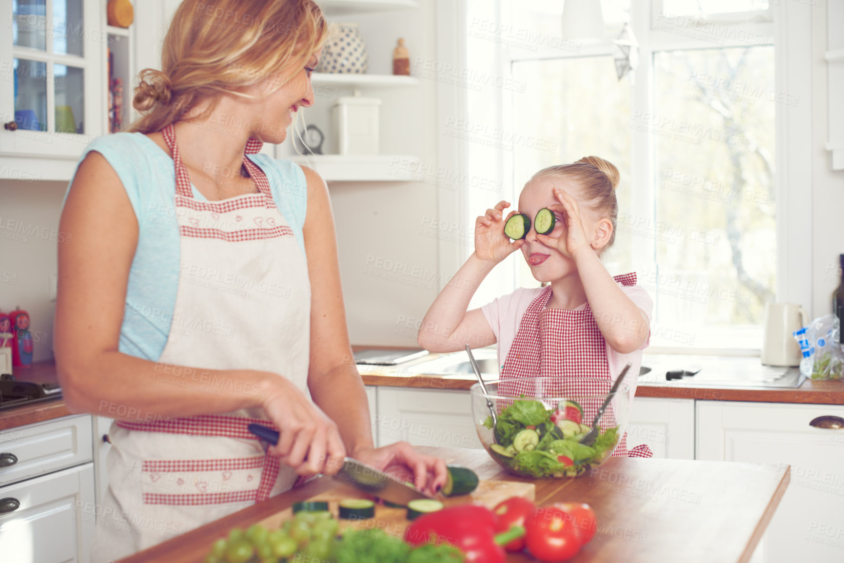 Buy stock photo Mother, girl and cucumber eyes in home, cooking and cutting vegetables for healthy salad in kitchen. Mama, daughter and funny joke or humor for nutrition, love and family preparation of vegan meal