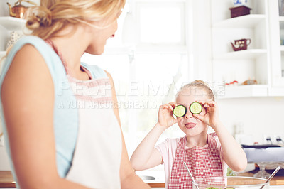 Buy stock photo Mother, girl and playful cooking in home, cucumber eyes and vegetables for healthy salad in kitchen. Mama, daughter and funny joke or humor for nutrition, love and family preparation of vegan meal