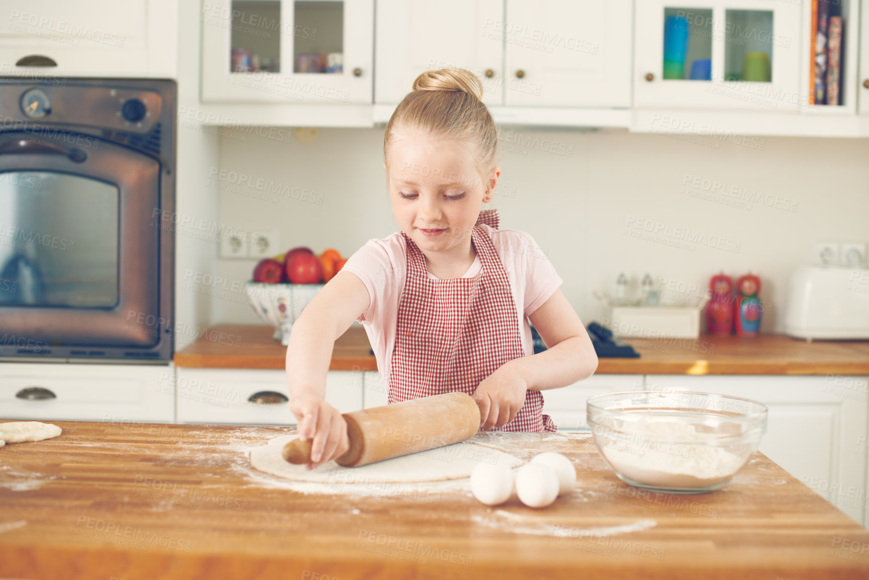 Buy stock photo Happy little girl baking in the kitchen at home. Cute child rolling out dough and learning to bake while working independently. Cooking promotes the development of learning and fine motor skills