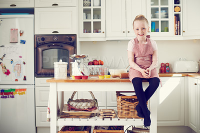 Buy stock photo A young girl learning to cook and bake in the kitchen inside a house. Smiling child sitting on top of a table growing up to be independent. Child development at home. Kid smiling preparing food alone