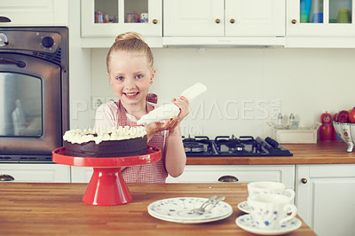 Buy stock photo Young child baking at home. Independent little girl learning to bake while decorating cake with a piping bag on the kitchen counter. Baking promotes the development of learning and fine motor skills