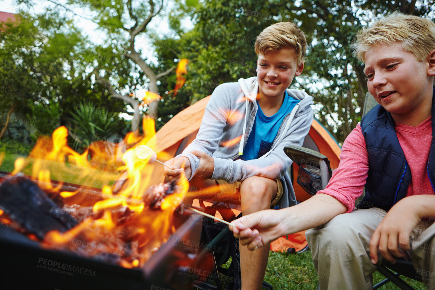 Buy stock photo Cropped shot of two young boys sitting by the campfire