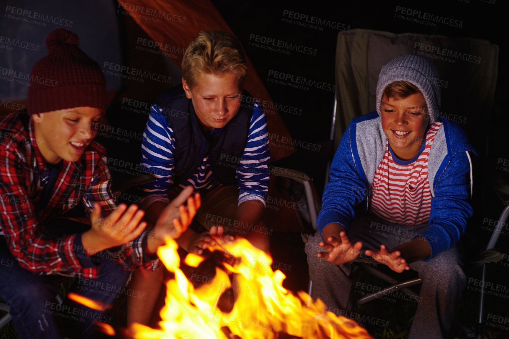 Buy stock photo Cropped shot of three young boys sitting by the campfire