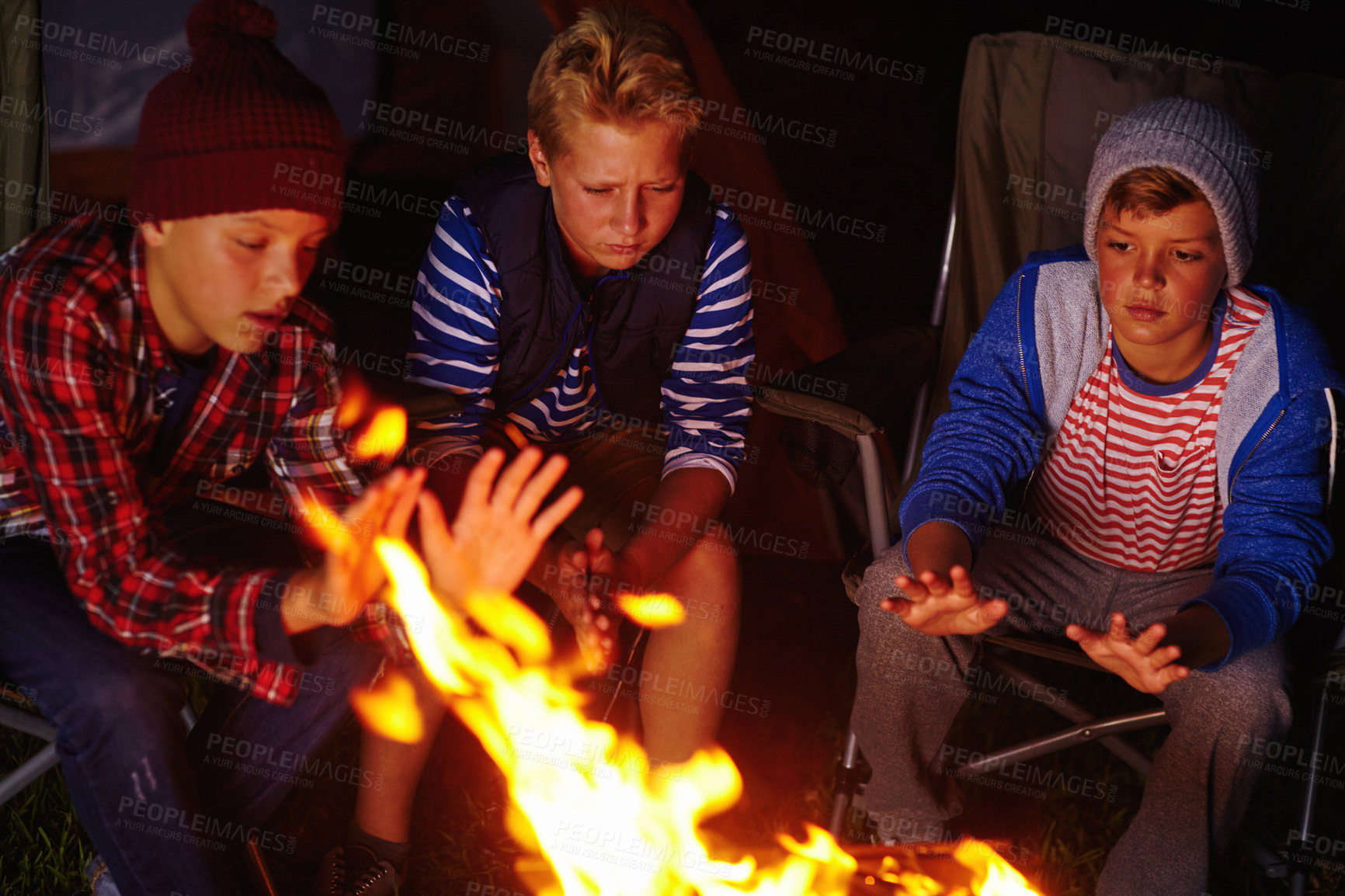 Buy stock photo Cropped shot of three young boys sitting by the campfire