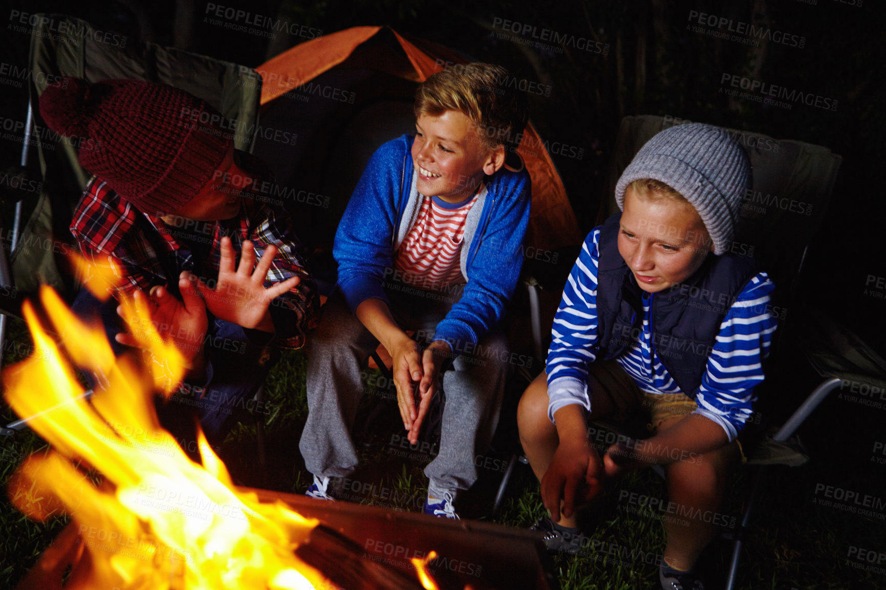 Buy stock photo Cropped shot of three young boys sitting by the campfire