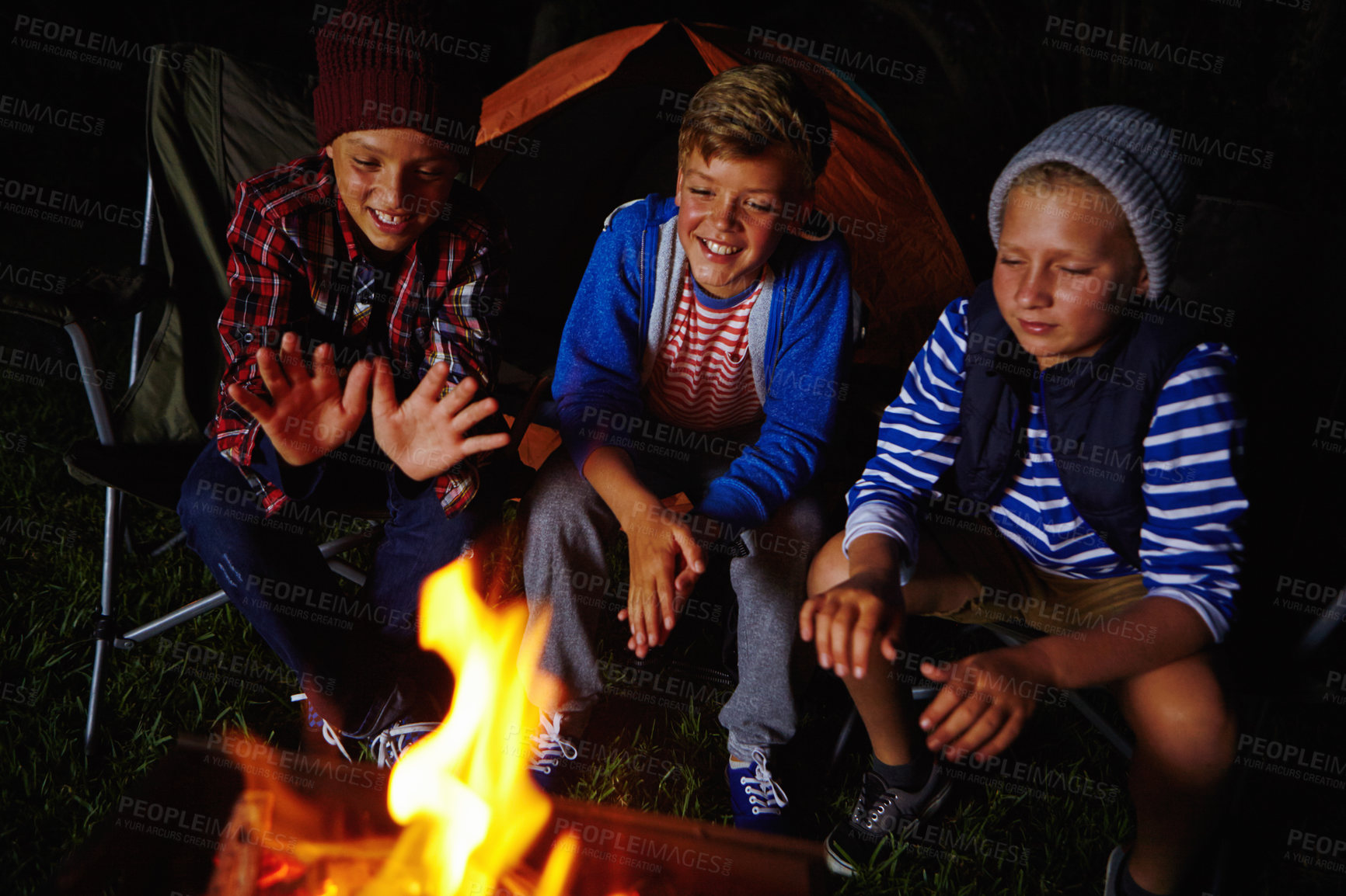 Buy stock photo Cropped shot of three young boys sitting by the campfire