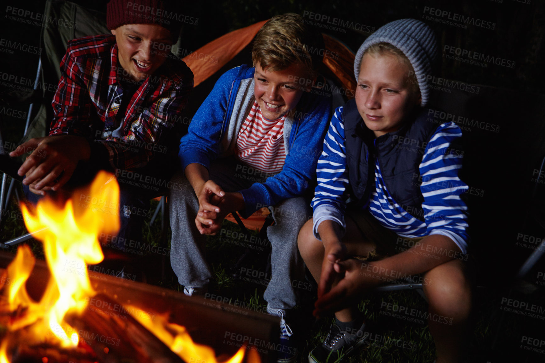 Buy stock photo Cropped shot of three young boys sitting by the campfire