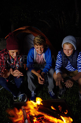 Buy stock photo Cropped shot of three young boys sitting by the campfire