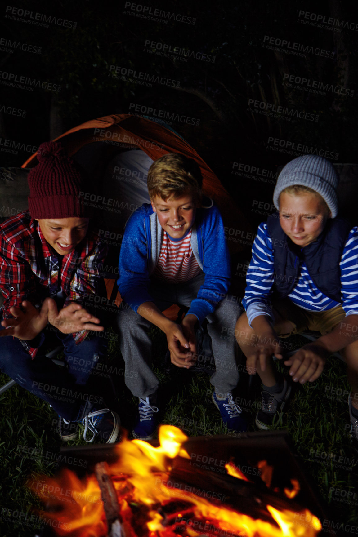 Buy stock photo Cropped shot of three young boys sitting by the campfire