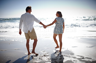 Buy stock photo Rearview of a happy mature couple walking hand in hand on the beach