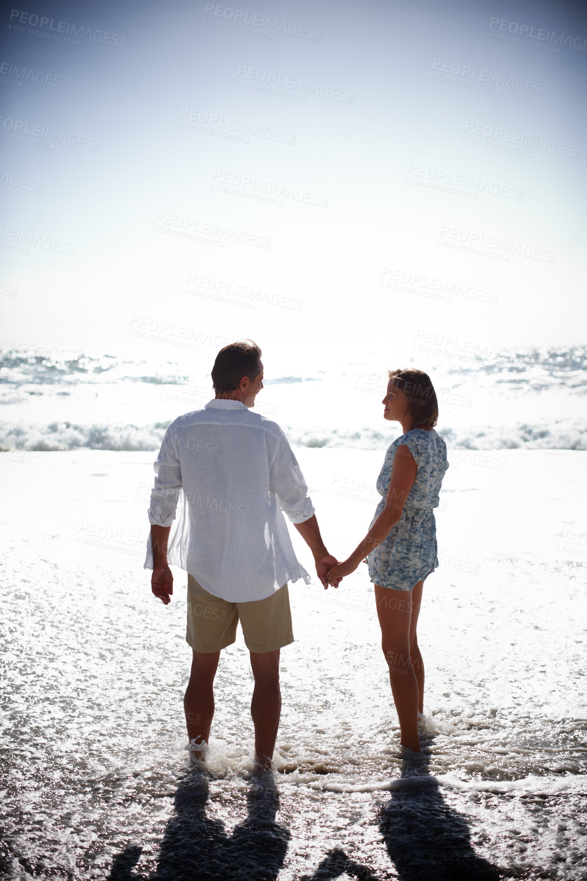 Buy stock photo Rearview of a happy mature couple walking hand in hand on the beach