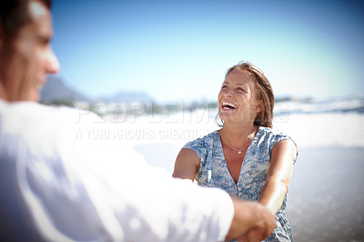 Buy stock photo A happy mature couple holding hands while facing each other on the beach