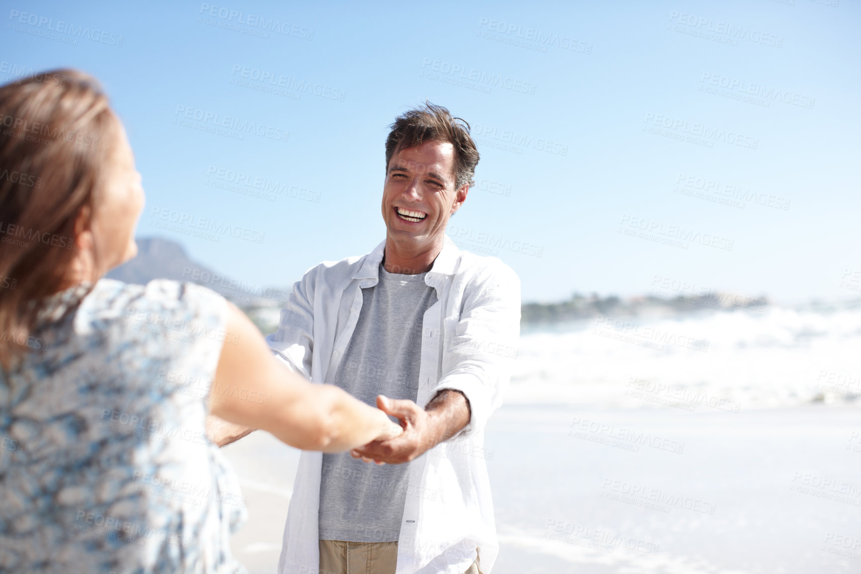 Buy stock photo A happy mature couple holding hands while facing each other on the beach