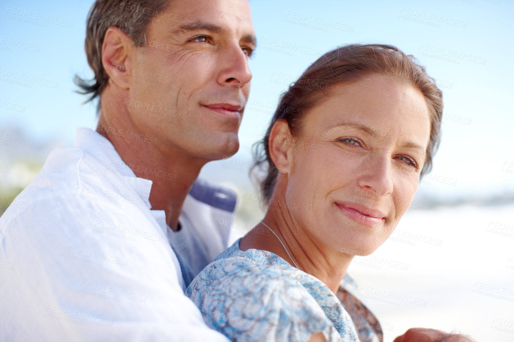 Buy stock photo Portrait of a mature man embracing his happy wife from behind as they stand on the beach