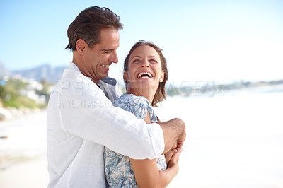 Buy stock photo A mature man embracing his happy wife from behind as they stand on the beach