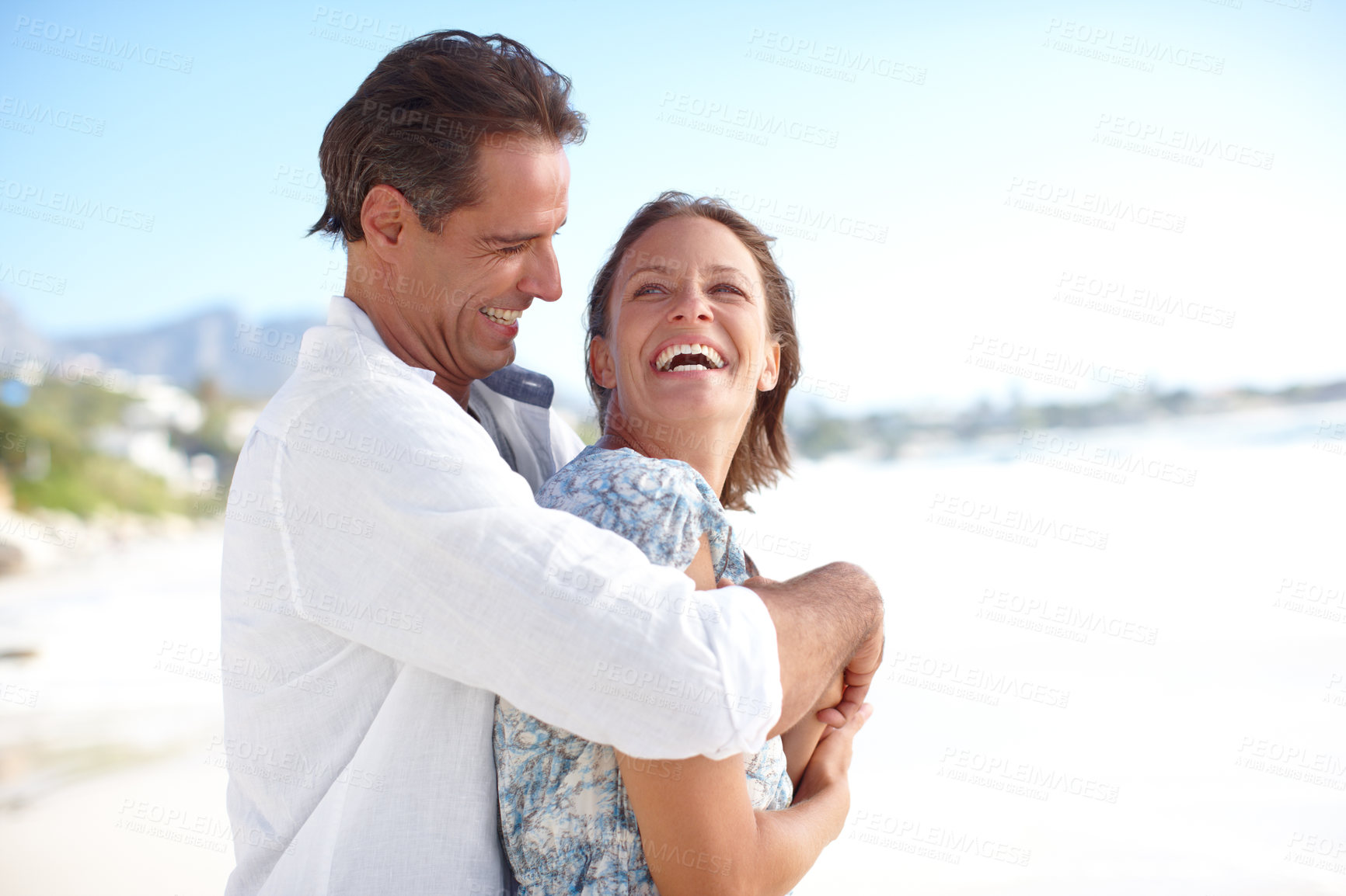 Buy stock photo A mature man embracing his happy wife from behind as they stand on the beach