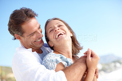 Buy stock photo A mature man embracing his happy wife from behind as they stand on the beach