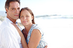 Portrait of a  mature man embracing his happy wife from behind as they stand on the beach