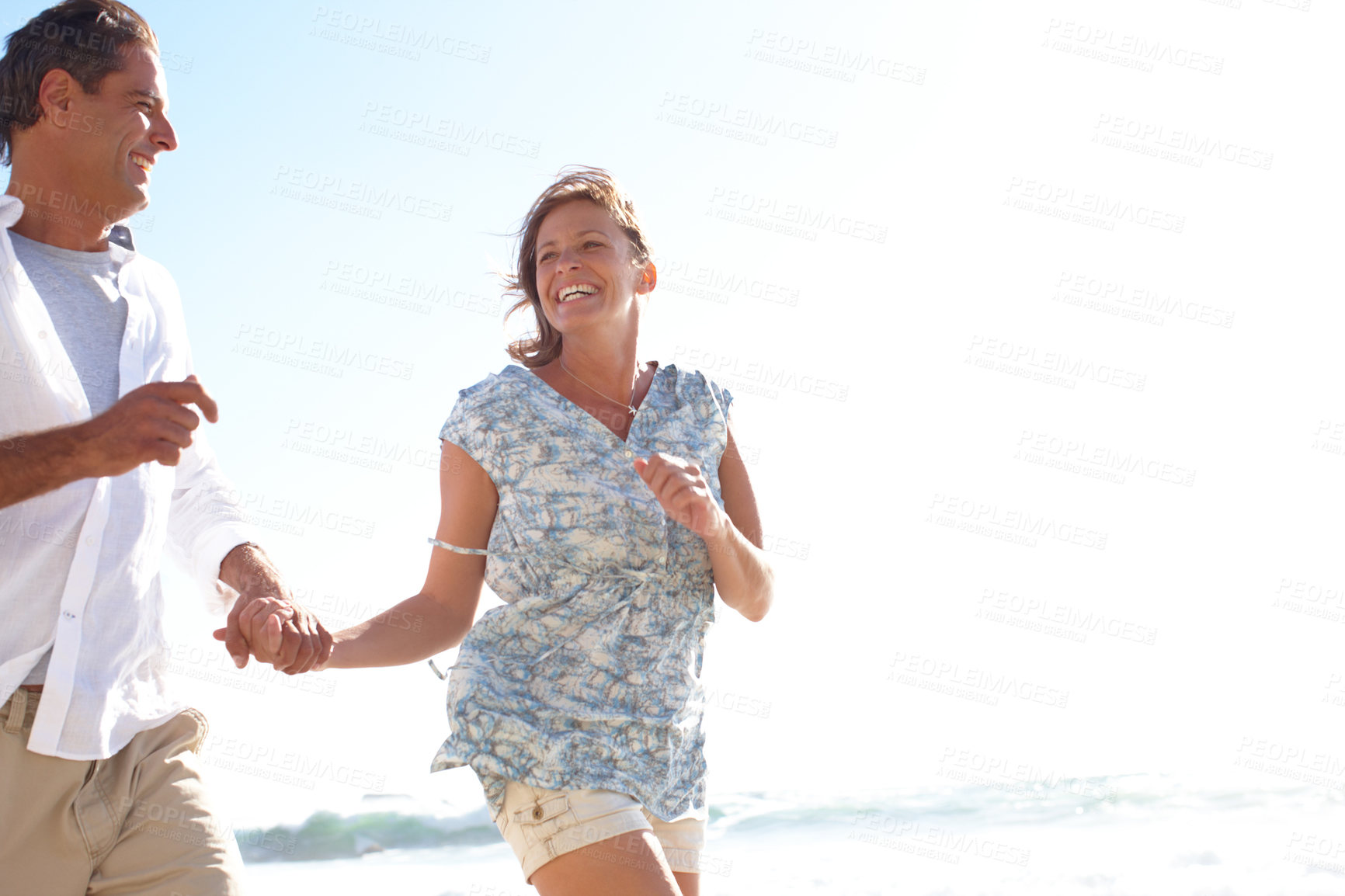 Buy stock photo A happy mature couple holding hands while running on the beach