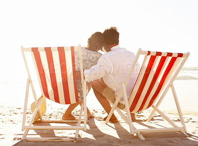 Buy stock photo Rear view of a couple embracing while sitting in deckchairs on the beach