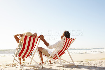 Buy stock photo A happy couple sitting in deck chairs on the beach together - Copyspace