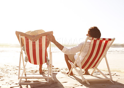 Buy stock photo Rear view of a couple sitting in deck chairs on the beach together