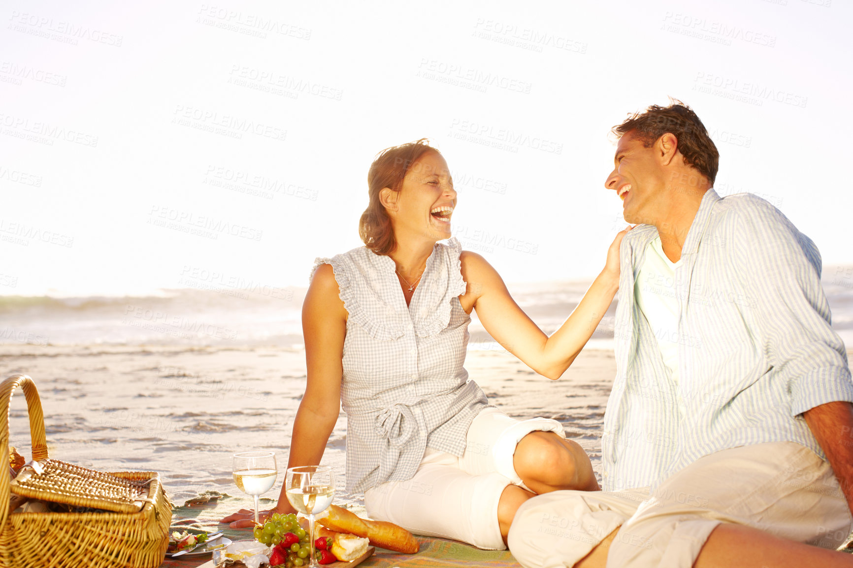 Buy stock photo Beach, couple and laughing on picnic with food for support, romance or love in Bali. Seaside, people and happy in relationship on holiday, anniversary and honeymoon for valentines day with wine glass