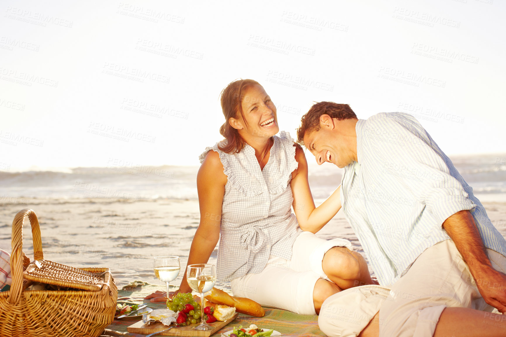 Buy stock photo Seaside, couple and laughing on picnic with wine glass for support, romance and love in Bali. Beach, people and happiness in relationship on holiday, anniversary and honeymoon for valentines day