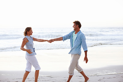 Buy stock photo A happy couple holding hands as the sunsets on the beach
