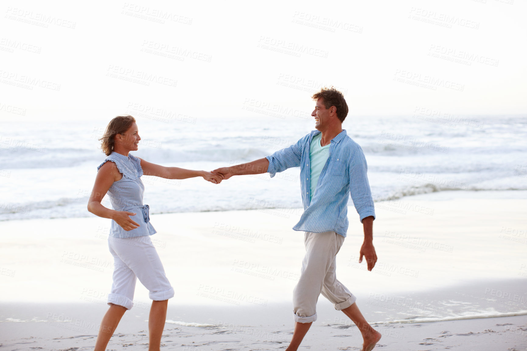 Buy stock photo A happy couple holding hands as the sunsets on the beach