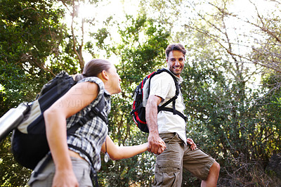 Buy stock photo Handsome hiker looking down at his girlfriend while pulling her up by the hand