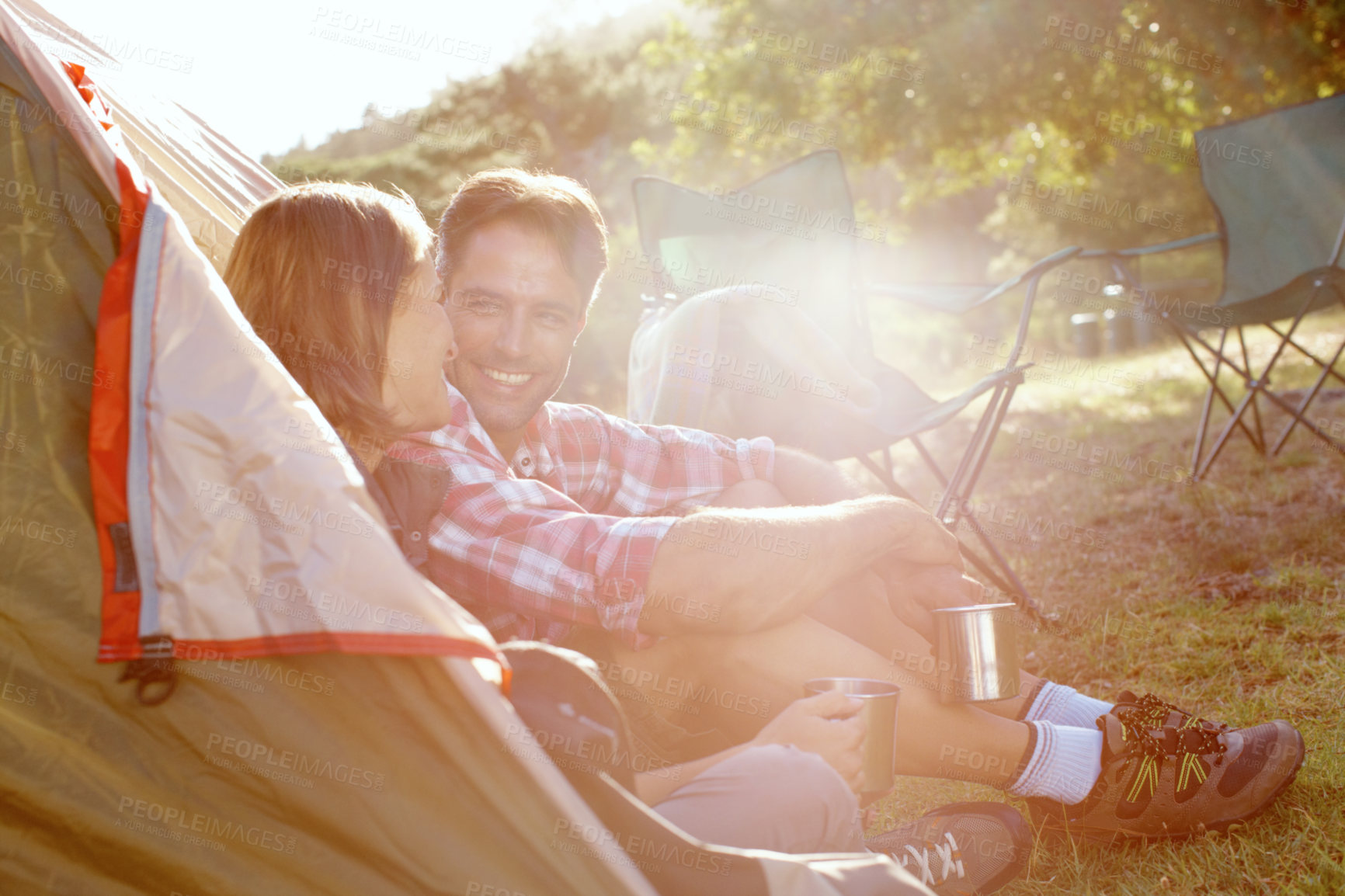 Buy stock photo Outdoor, couple and happy by tent for camping, holiday and travel vacation with bonding in wilderness. Nature, man and woman with admiration for commitment, adventure and love with coffee by flare