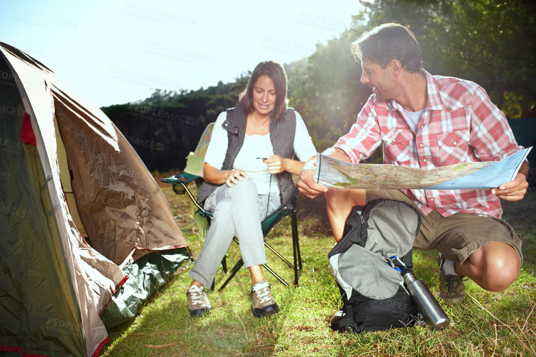 Buy stock photo Couple, camping and reading map by tent on adventure with woman, man and talking on grass in nature. People, chart and navigation with route, trekking and happy with direction for vacation in Germany