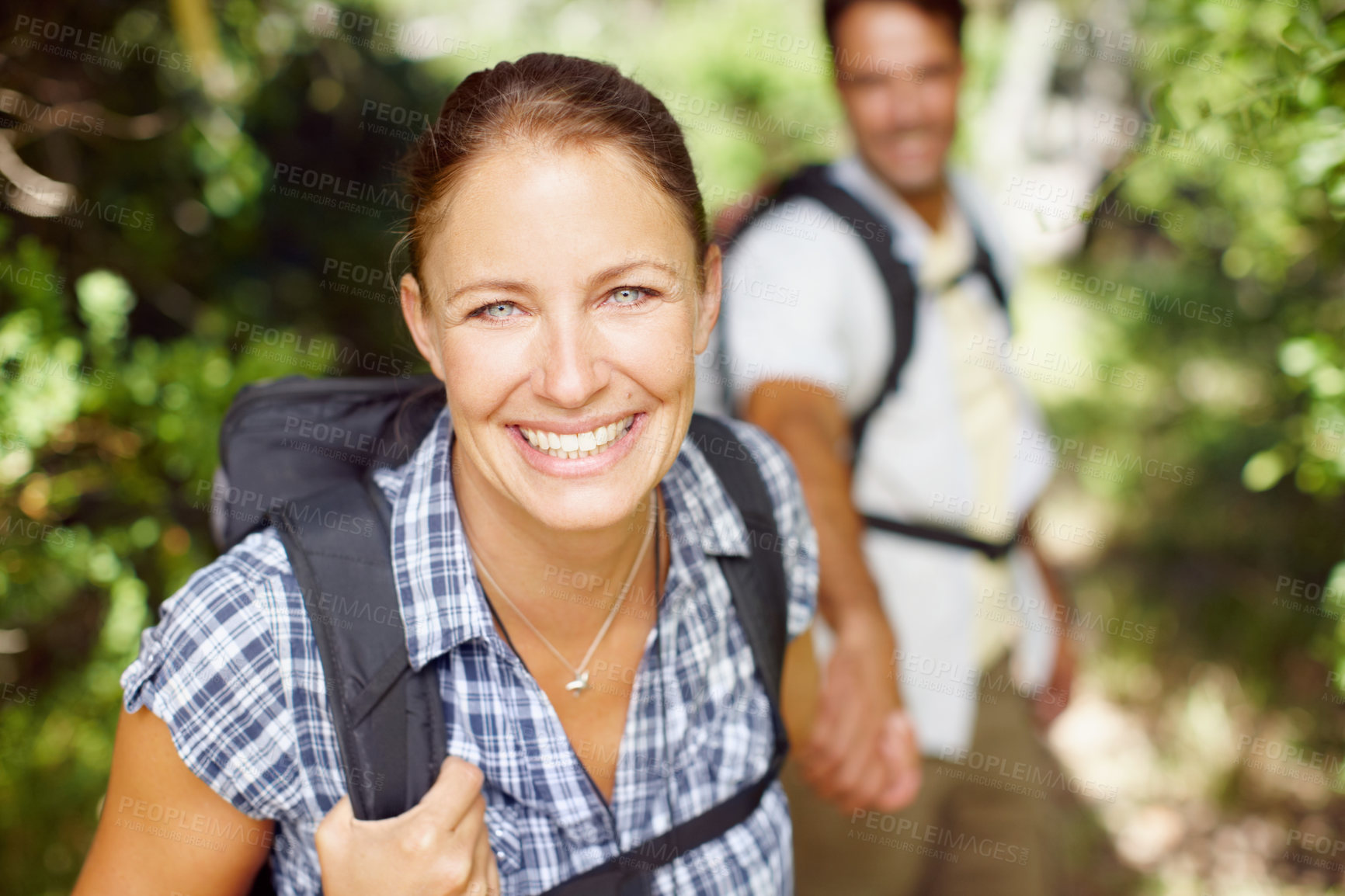 Buy stock photo Portrait of a young woman wearing a backpack with her husband in the background