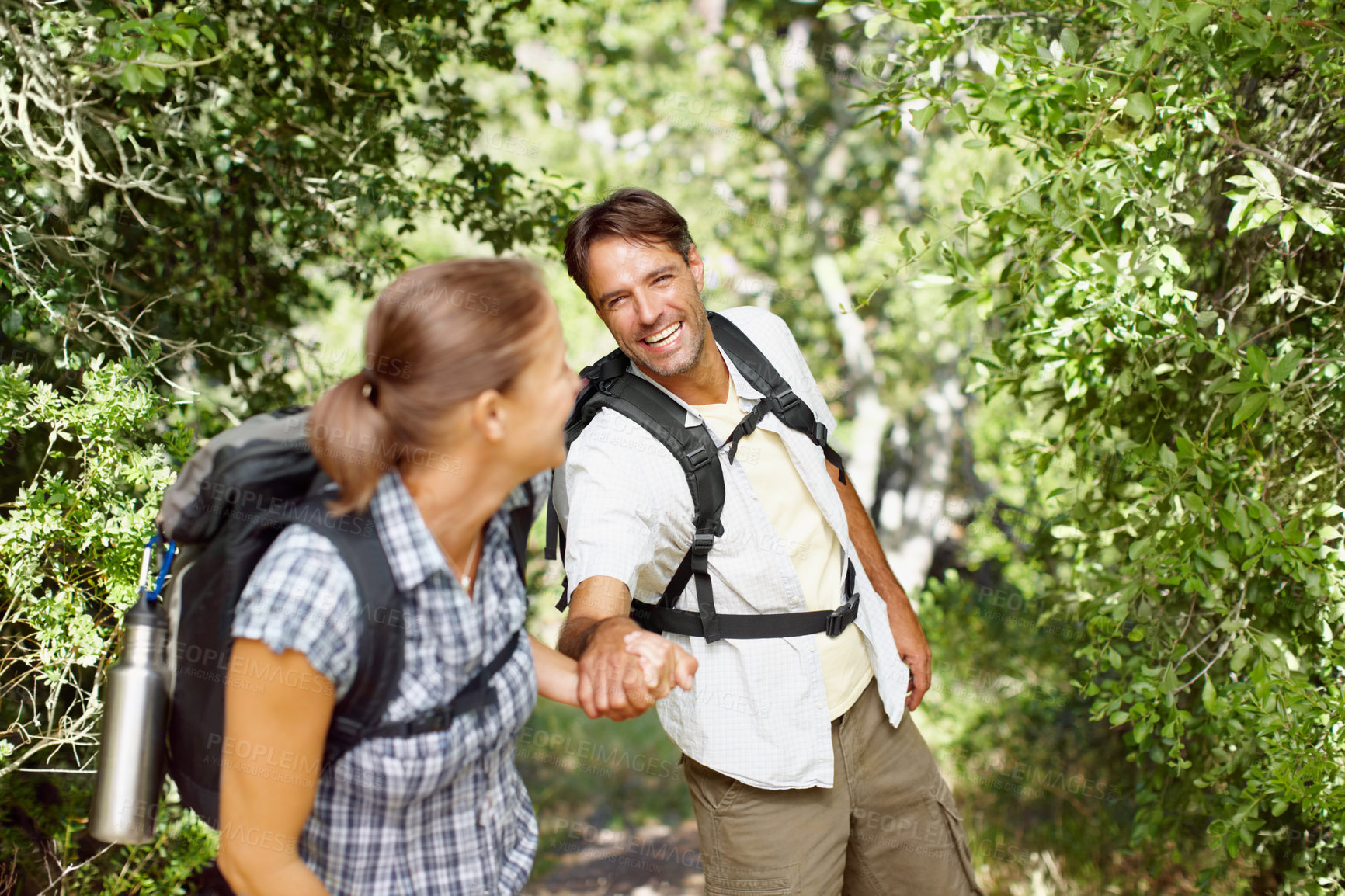 Buy stock photo A young man being pulled playfully by his wife with backpacks on their backs