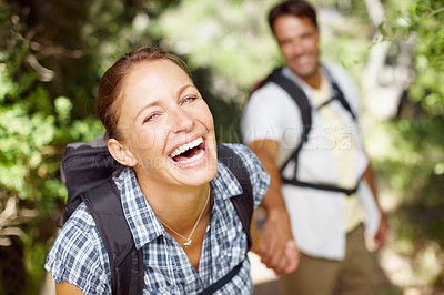 Buy stock photo Portrait of a young woman laughing and wearing a backpack with her husband in the background