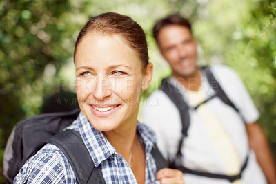 Buy stock photo A young woman smiling and wearing a backpack with her husband in the background