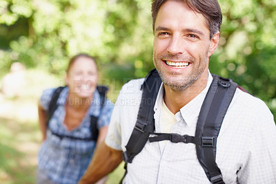 Buy stock photo Portrait of a young man with a backpack smiling with his wife in the background