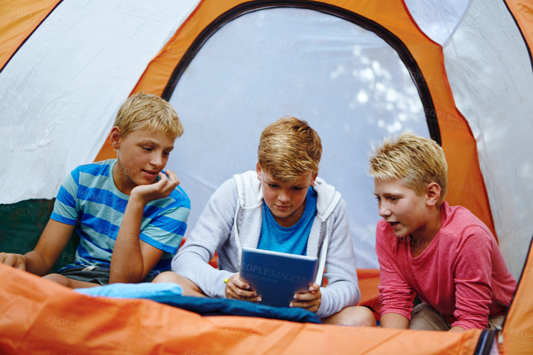 Buy stock photo Shot of three young boys using a digital tablet while in their tent