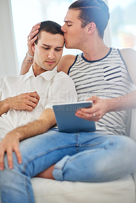 Buy stock photo Shot of an affectionate gay couple using a digital tablet while relaxing on the sofa at home