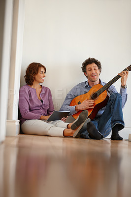 Buy stock photo Shot of a woman using her digital tablet while her husband plays the guitar